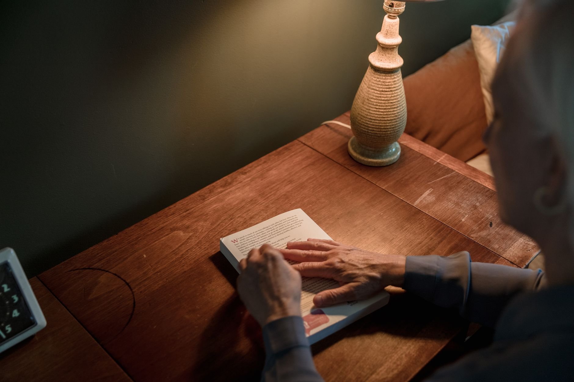A person reads a book at a warm lamp-lit desk.